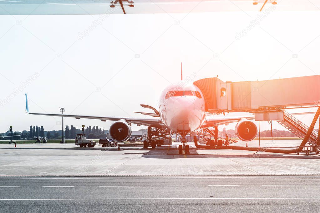 Big modern commercial plane on airfield docked with boarding bridge at sunrise or sunset. Blue clear sky on background. Travel and tourist destination concept