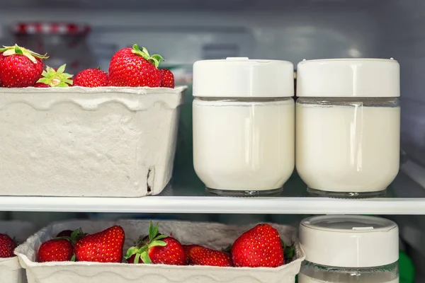 Refrigerator shelf with organic juicy strawberries in bio recycled paper boxes and homemade natural milk yogurt. Fridge filled with berries in cardboard containers. Healthy and eco friendly food diet