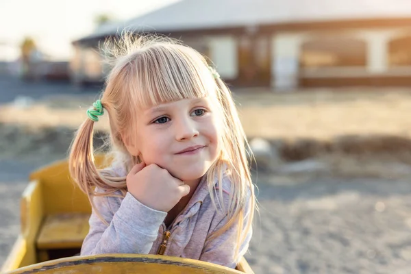 Urocza cute kaukaski blond Kid Girl portret siedzi w drewnianym wózku, patrząc na bok i marzy w gospodarstwie lub parku podczas ciepłej jesieni wieczorem — Zdjęcie stockowe