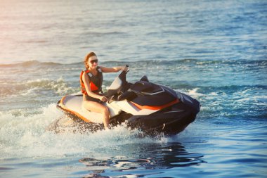 Young adult sporty caucasian woman riding jet ski in ocean blue water at warm evening sunset. Beach extreme sport activities and recreation clipart