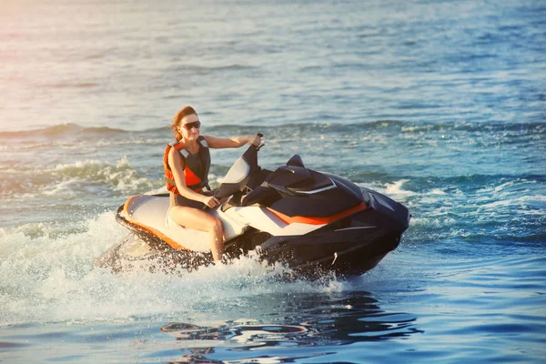 Genç yetişkin sportif beyaz kadın sıcak akşam gün batımında okyanus mavisu jet ski sürme. Plaj ekstrem spor aktiviteleri ve rekreasyon