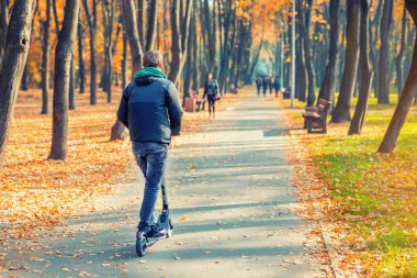 Güzel renkli sonbahar Şehir Parkı boyunca modern elektrikli scooter sürme Genç yetişkin kişi. Adam çok renkli sonbahar ağacı Vadisi aracılığıyla Gadget araç sürüş