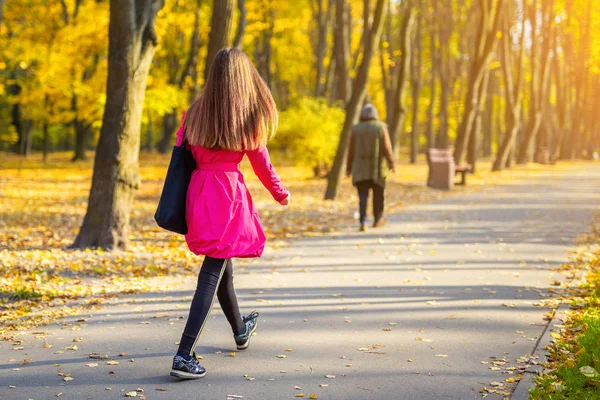 Jovem mulher adulta em casaco casual brilhante andando ao longo do belo beco do parque de outono de cor dourada. Menina desportiva atraente feliz no parque da cidade ou estrada da floresta. Fundo natural sazonal — Fotografia de Stock