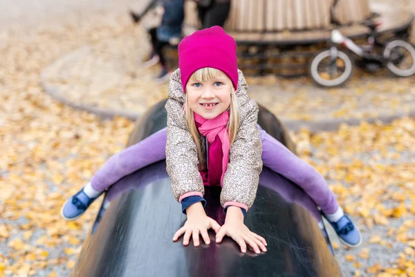 Retrato de una linda niña rubia caucásica divirtiéndose jugando en un moderno parque al aire libre en el parque de la ciudad en otoño. Adorable niño feliz disfrutando y sonriendo durante las actividades de ocio —  Fotos de Stock