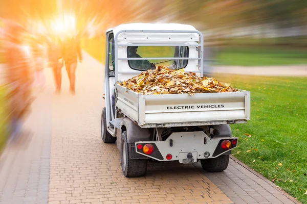 Kleine elektrische truck het verwijderen van gevallen bladeren in het lichaam in de herfst City Park. Gemeentelijke stedelijke diensten met behulp van ecologie groene voertuig vrachtwagen schoon straten van loof — Stockfoto