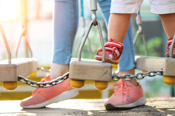 Fiatal felnőtt anya, kis aranyos kisgyermek gyerek szórakozik élvező szabadidős játékok szabadtéri játszótér világos napsütéses napon. Anya gondozása és támogatása gyerek így az első lépéseket. Gyermek sportfoglalkozások — Stock Fotó