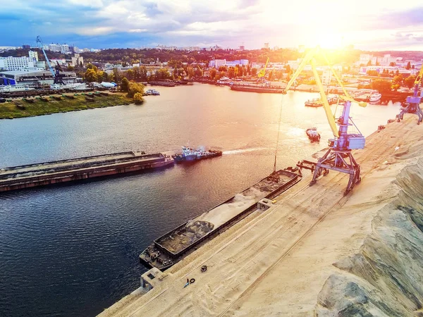 Aerial view of heavy crane loading bulk goods at Dnieper river cargo port terminal in Kiev at evening sunset time. tugboat pushes barge with sand after loading. Industrial inland navigation — Stock Photo, Image