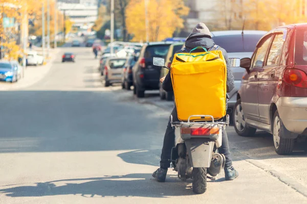 Доставка еды курьер с большим желтым рюкзаком верхом скутер на городской улице с движением. Быстрая доставка еды на обед. Подростковая работа — стоковое фото