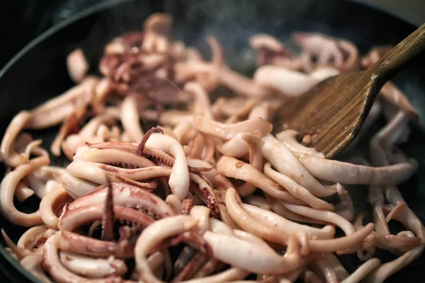 Close-up frying pan cooking baby squid and octopus. Wooden kitchen spatula mixing ingridients while preparing frying calamari traditional italian seafood meal — Stock Photo, Image