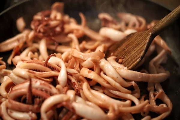 Close-up frying pan cooking baby squid and octopus. Wooden kitchen spatula mixing ingridients while preparing frying calamari traditional italian seafood meal — Stock Photo, Image