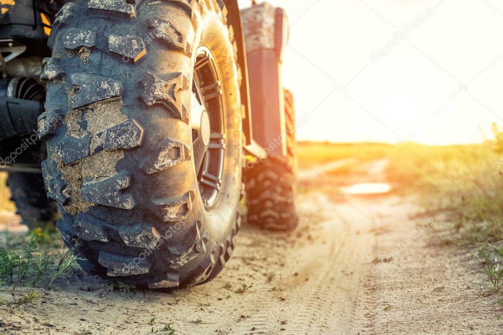 Close-up tail view of ATV quad bike on dirt country road at evening sunset time. Dirty wheel of AWD all-terrain vehicle. Travel and adventure concept.Copyspace.Toned