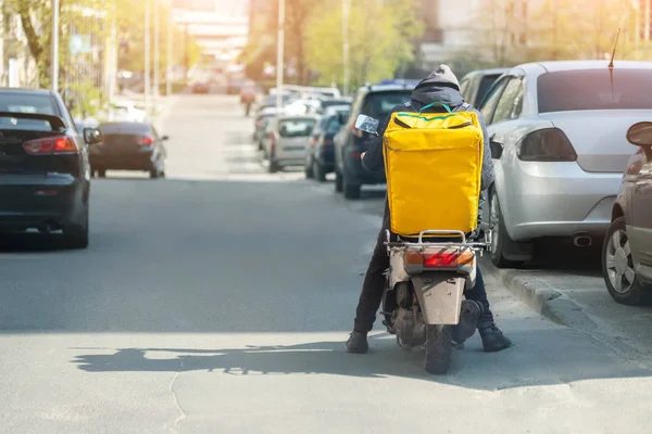 Correio de entrega de alimentos com grande mochila amarela montando scooter na rua da cidade com tráfego. Almoço rápido entrega takeaway. Trabalho de adolescente — Fotografia de Stock