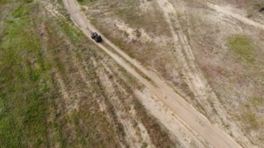 Kuru sonbahar çim ve yeşil kozalaklı ağaç orman çayırları ile ülke engebeli arazi yolu üzerinde bir Atv dört bisiklet sürme genç yetişkin adam Yukarıdan aşağıya havadan görünümü. Macera sporu aktivite konsepti.