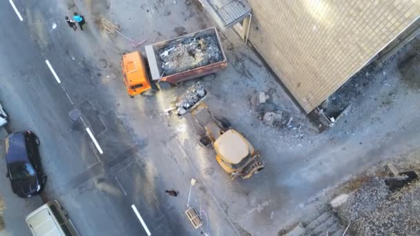 Pemuat Bulldozer mengunggah sampah dan puing-puing ke dalam truk sampah di lokasi konstruksi dekat jalan raya. Membongkar bangunan dan jasa pembuangan limbah konstruksi. Latar belakang industri drone udara — Stok Video