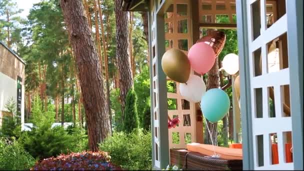 Gäng olika färgglada helium Luftballonger spelar på vinden knuten till trä utomhus lusthus terrass som dekoration för barn bithday Party. Jubileumsfest inredning design — Stockvideo