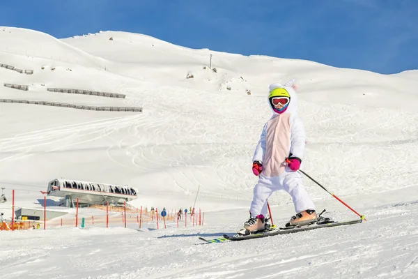 Cute adorable preschooler caucasian kid girl portrait with ski in helmet, goggles and unicorn fun costume enjoy winter sport activities. Little child skiing on luxury alpine resort in mountains — Stock Photo, Image