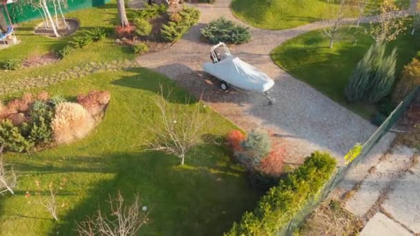 Aerial Drone vy över täckt båt parkerad på trailer på Backyard Garden med cirkelbana, gröna gräsmatta kullar och fruktträd. Landskapsplanering och trädgårdsskötsel. Höstlandskap — Stockvideo