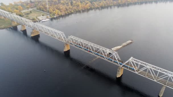 Мальовничий міський пейзаж Києва та Дніпра на заході сонця. Буксир з підтримкою баржі з піском Сипучі матеріали прямуючи по річці Дніпро під залізничним мостом з переїзним поїздом — стокове відео