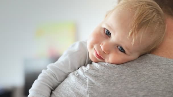 Close-up portrait of cute adorable blond caucasian toddler boy on fathers shoulder indoors. Sweet little child smiling feeling safety on daddys hand. Responsibility and childcare. happy childhood — Stock Video