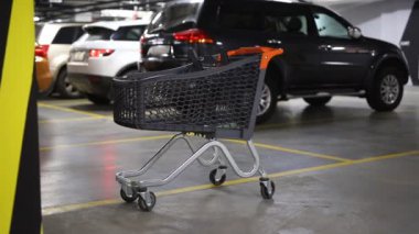 Modern plastik alışveriş sepeti sol alışveriş merkezi çatılı yer altı otoparkı, boş. Arka plan üzerinde bulanık park edilmiş arabalar ile süpermarket arabası. Rahat rahat ve alışveriş İmkanları