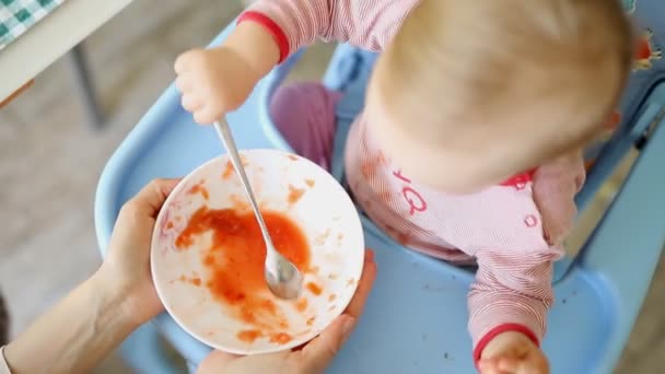 愛らしいかわいい白人のブロンドの幼児の男の子は、キスン屋内の椅子でおいしい野菜スープを食べます。母親はスプーンで赤ちゃんの健康的な食べ物を供給しています。自然な子供の栄養と食事 — ストック動画