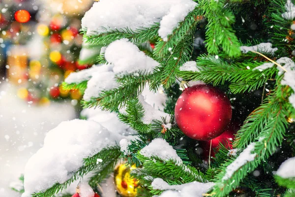 Közelkép karácsonyfa színes dekorációs labda, hópelyhek és hó lucfenyő ágak alatt hóesés télen a szabadban. Szilveszter ünnep szezon háttér koncepció — Stock Fotó