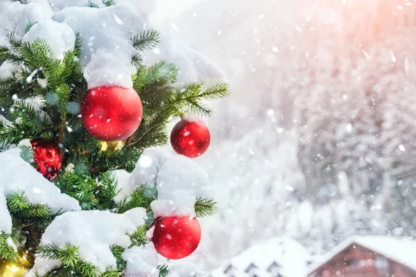 Közelkép karácsonyfa színes dekorációs labda, hópelyhek és hó lucfenyő ágak alatt hóesés télen a szabadban. Szilveszter ünnep szezon háttér koncepció — Stock Fotó