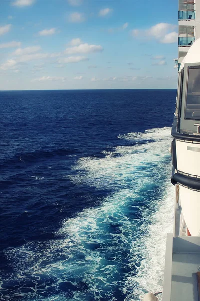 Vue latérale depuis le pont du balcon du grand bateau de croisière naviguant sur l'océan ou la mer et laissant des sentiers tourbillonnants et tourbillonnants avec un ciel bleu en arrière-plan. Voyages et vacances. Aventure voyage début concept — Photo