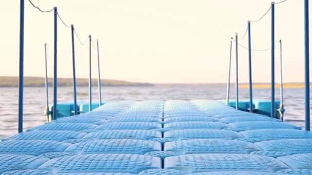 Muelle de pontón de plástico flotante azul con barandillas de cuerda balanceándose sobre las olas en la playa del lago o río. Muelle para botes pequeños y pasarela de personas — Vídeos de Stock