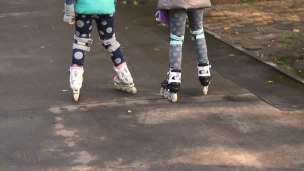 Dos lindas niñas caucásicas que se divierten montando patines en el parque de la ciudad por la acera de asfalto mojado después de la lluvia en otoño o primavera. Jóvenes novias divirtiéndose juntas al aire libre — Vídeo de stock