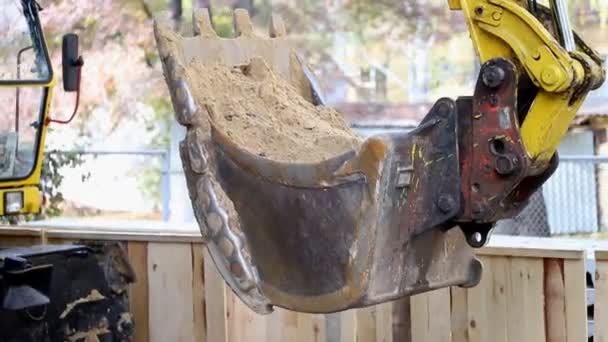 Nahaufnahme-Bagger fährt mit voll beladener Schaufel mit Erde durch Baustelle — Stockvideo