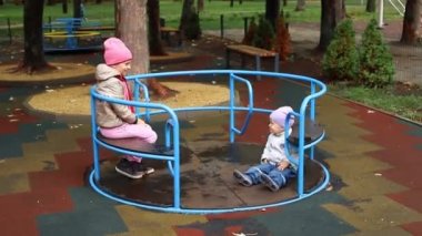 İki şirin beyaz kardeş, sonbaharda şehir parkında yağmurdan sonra ıslak çocuk parkında dönme dolambaçlı dönen atlı karıncaya binerek eğleniyorlar. Erkek ve kız kardeş dışarıda oynamaktan hoşlanırlar.