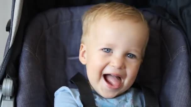 Lindo adorable niño rubio caucásico feliz sentado en el cochecito y riendo jugando buscar y ocultar juego. divertido alegre niño indulges y mostrando lengua — Vídeos de Stock