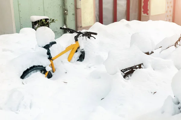 Kolo pokryté velkou silnou sněhovou vrstvou po sněhové bouři na evropské městské ulici v zimě. Opuštěné kolo pohřbené ve sněhové bouři poblíž budovy za chladného počasí. Scénická sezónní pozadí — Stock fotografie