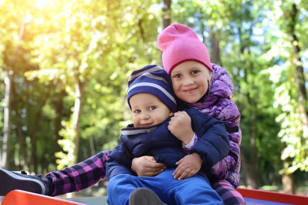Dwa słodkie adorable zabawy kaukaskie rodzeństwo chłopiec dziewczyna dziecko cieszyć się zabawy na placu zabaw na podwórku lub w parku miejskim na świeżym powietrzu. Mały braciszek z siostrzanym portretem przytulający się i uśmiechający. Opieka rodzinna — Zdjęcie stockowe