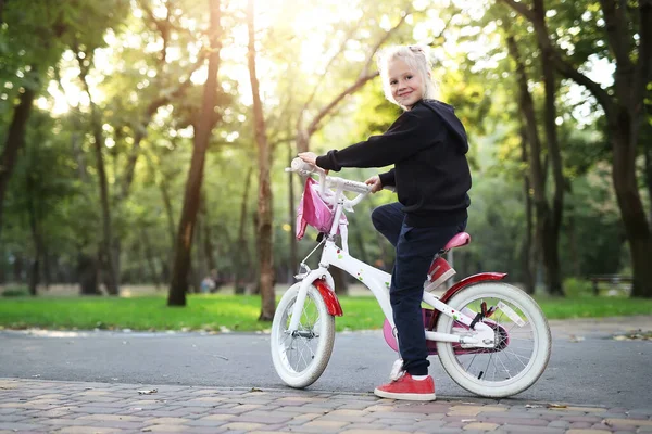 可爱的美丽的高加索金发小女孩喜欢在阳光明媚的室外，沿着绿色夏季城市公园森林或花园的小径骑着白色的小自行车。儿童健康生活方式概念 — 图库照片