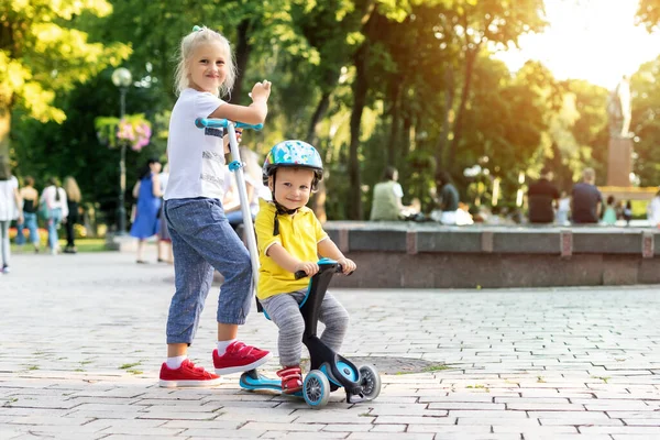 Két aranyos kis kaukázusi testvér fiú sisakban és lány szórakozás lovaglás háromkerekű egyensúly fut kerékpár robogó a városi parkban vagy erdőben. Első bicikli. Gyerekek szabadtéri sportolási lehetőségek — Stock Fotó