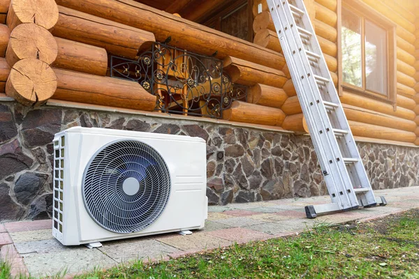 Новый современный компрессорный блок кондиционирования воздуха HVAC, подготовленный к установке или замене рядом со стеной деревянного бревенчатого коттеджа. Лестница и оборудование для обслуживания и обслуживания — стоковое фото