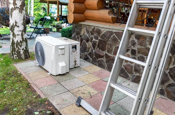 Nueva unidad de compresor externo de aire acondicionado HVAC moderna preapred para la instalación o reemplazo cerca de la pared de madera casa de campo residencial de troncos. Escalera y equipo para servicio y mantenimiento —  Fotos de Stock