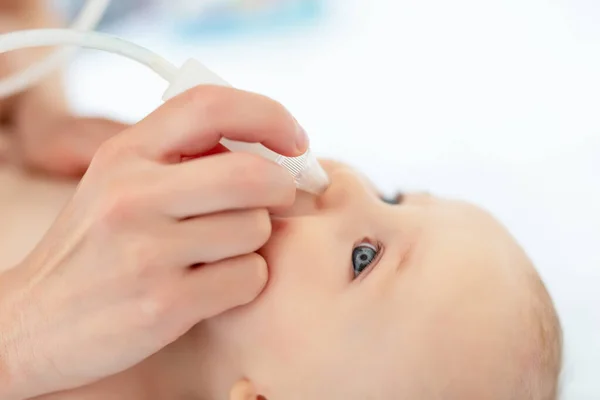 小宝宝的妈妈用吸气器和医疗工具在家里为可爱的男婴擦拭流鼻涕。婴儿父母保健和爱的概念 — 图库照片