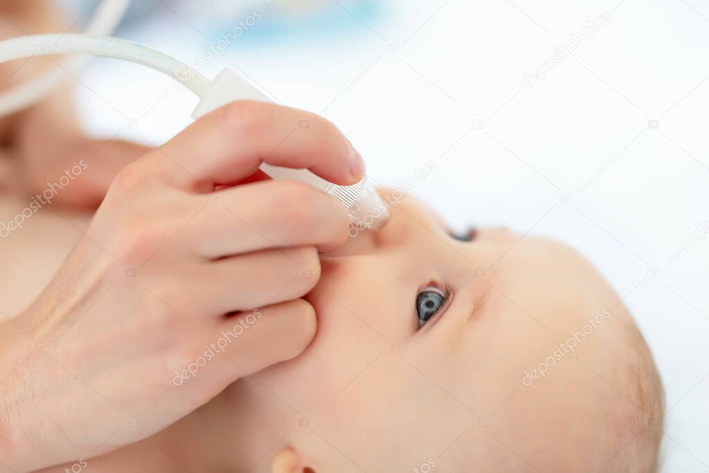 Closeup mother hand with aspirator medical tool cleaning runny nose of cute infant newborn baby boy son at home indoors. Baby parent health care and love concept