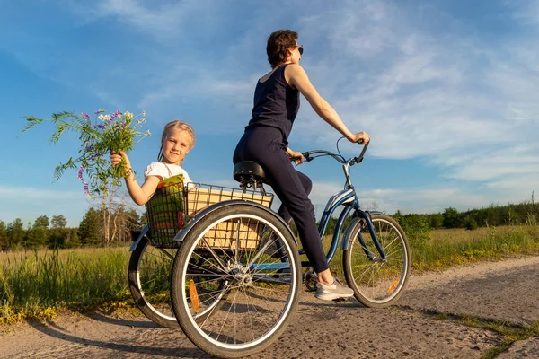 Fiatal felnőtt kaukázusi anya élvezi, hogy szabadidős szórakoztató lovaglás kerékpár aranyos imádnivaló szőke lánya gazdaság vad mező virág festői vidéki országút fényes napos napon. Vidéki vakáció — Stock Fotó