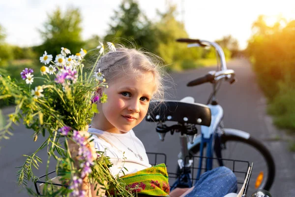 Портрет милый очаровательный кавказский блондинка маленькая девочка пользуются досуг весело кататься на велосипеде с семьей проведения дикого полевого цветка на живописной сельской дороге в яркий солнечный день. Отпуск за городом — стоковое фото