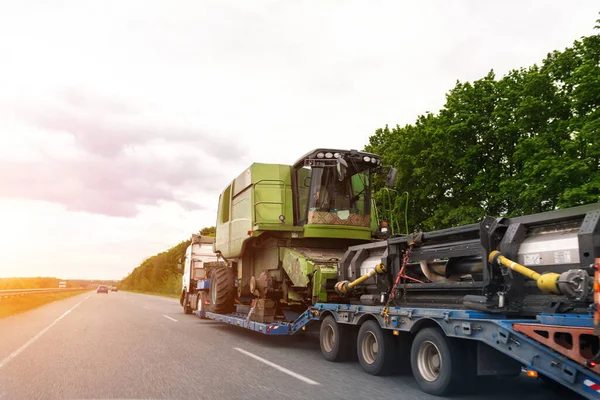 Camión industrial pesado con semirremolque plataforma de transporte desmontado cosechadora cosechadora cosechadora en carretera común carretera en el atardecer o amanecer día. Servicio de transporte de equipos agrícolas —  Fotos de Stock