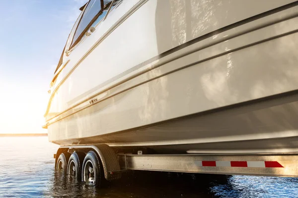 Stor lyx stuga motorbåt kryssare yacht sjösättning på släpvagn ramp på flod eller sjö. Varm morgon soluppgång solsken reflektion i lugnt vatten yta. Lyxigt rikt fiske fritid rekreation livsstil — Stockfoto