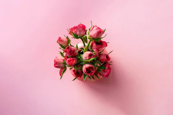 Above top view of minimalist tender small pink rose flower bouquet in little ceramic vase on pastel background. Flat lay vintage retro stylish handmade artwork floral decoration