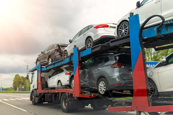 Tow truck car carrier semi trailer on highway carrying batch of damaged cars sold on insurance car auctions for repair and recovery. Vehicles shipment and rescue service — Stock Photo, Image