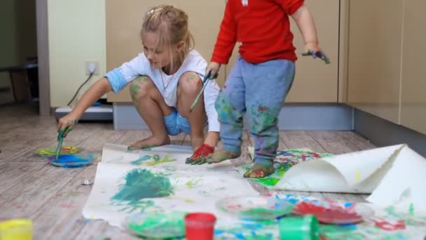 Αξιολάτρευτα χαριτωμένα καυκάσια μικρά ξανθά αδέλφια παιδιά απολαμβάνουν τη διασκέδαση μαζί με τη μητέρα ζωγραφική βούρτσα και την παλάμη στο σπίτι σε εσωτερικούς χώρους. Χαρούμενα χαρούμενα παιδιά χαμογελώντας σχέδιο αριστούργημα τέχνης εικόνα — Αρχείο Βίντεο