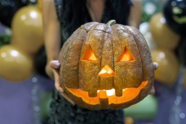 Genç, yetişkin bir kadın, el yapımı, tuhaf, el yapımı, oyma yüzlü, parlak mumlu ya da içinde ışık olan bir balkabağı kafasıyla el ele tutuşuyor. Cadılar Bayramı partisi dekorasyonu geleneksel sonbahar tatilini kutladı