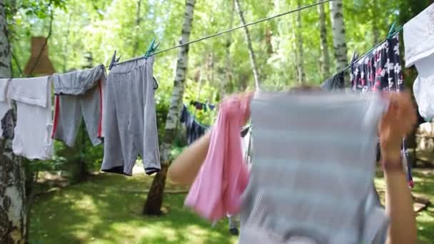 Candid real life portrait of young adult beautiful attractive caucasian woman hang up fresh washed family clothes on birch tree clothesline with pins at home yard on bright sunny day outdoor — Vídeo de Stock